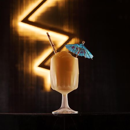 The Palazzo At The Venetian Hotel Las Vegas Exterior photo The photo shows a beautifully presented cocktail in a clear glass. The drink has a creamy, light brown color and is topped with a small blue paper umbrella for decoration. There is also a straw placed in the glass. The background features a dark, ill