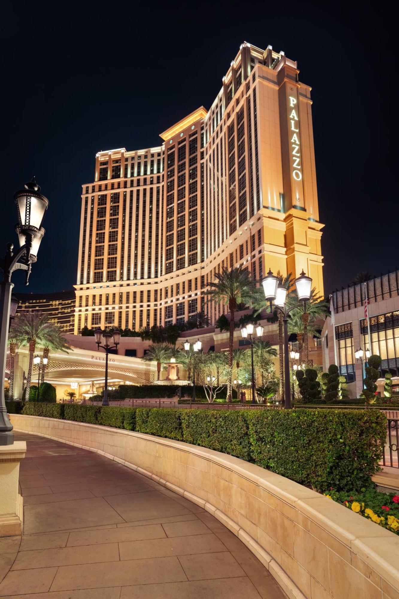 The Palazzo At The Venetian Hotel Las Vegas Exterior photo The photo depicts a large, illuminated hotel building at night. The architecture is modern and elegant, featuring tall structures with decorative lighting. Surrounding the hotel are neatly trimmed hedges and palm trees, contributing to a luxurious at
