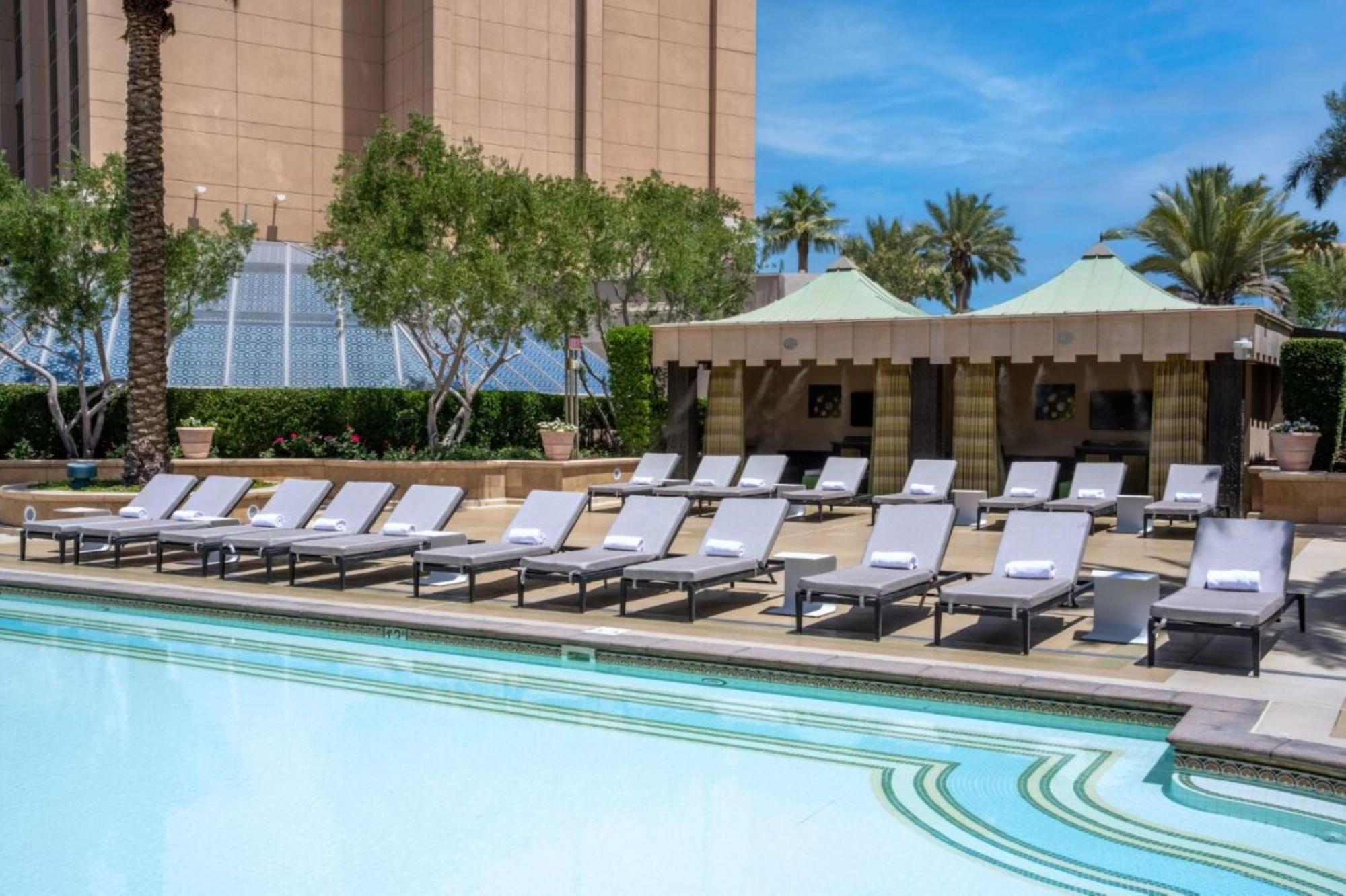The Palazzo At The Venetian Hotel Las Vegas Exterior photo The photo shows a tranquil outdoor pool area, featuring several modern lounge chairs arranged neatly by the water's edge. The pool has a clear blue surface, reflecting the sky. In the background, there are palm trees and some greenery, suggesting a t